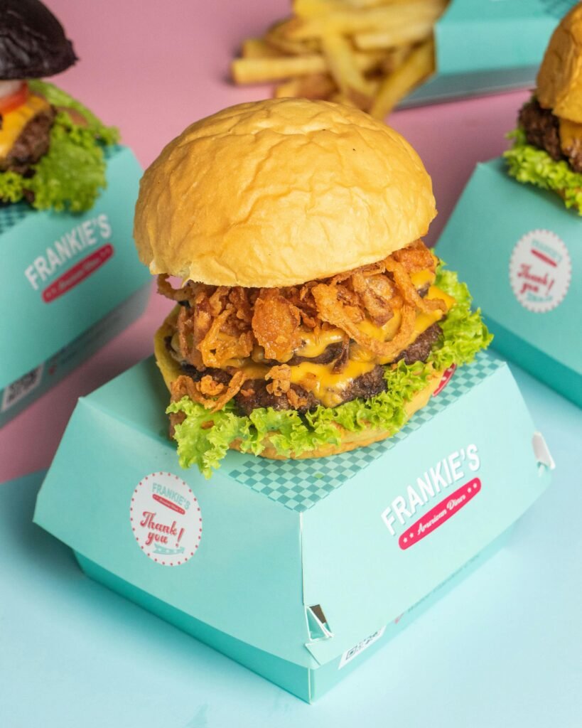 Close-up of a gourmet burger with onion rings and lettuce, served in a turquoise box.