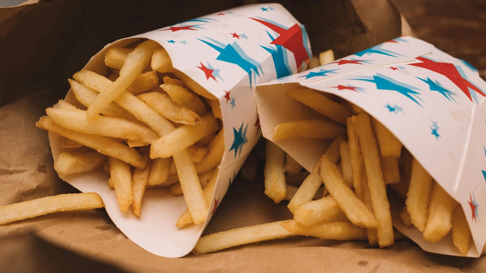 Golden crispy French fries in colorful star-patterned paper wrap on brown parchment.