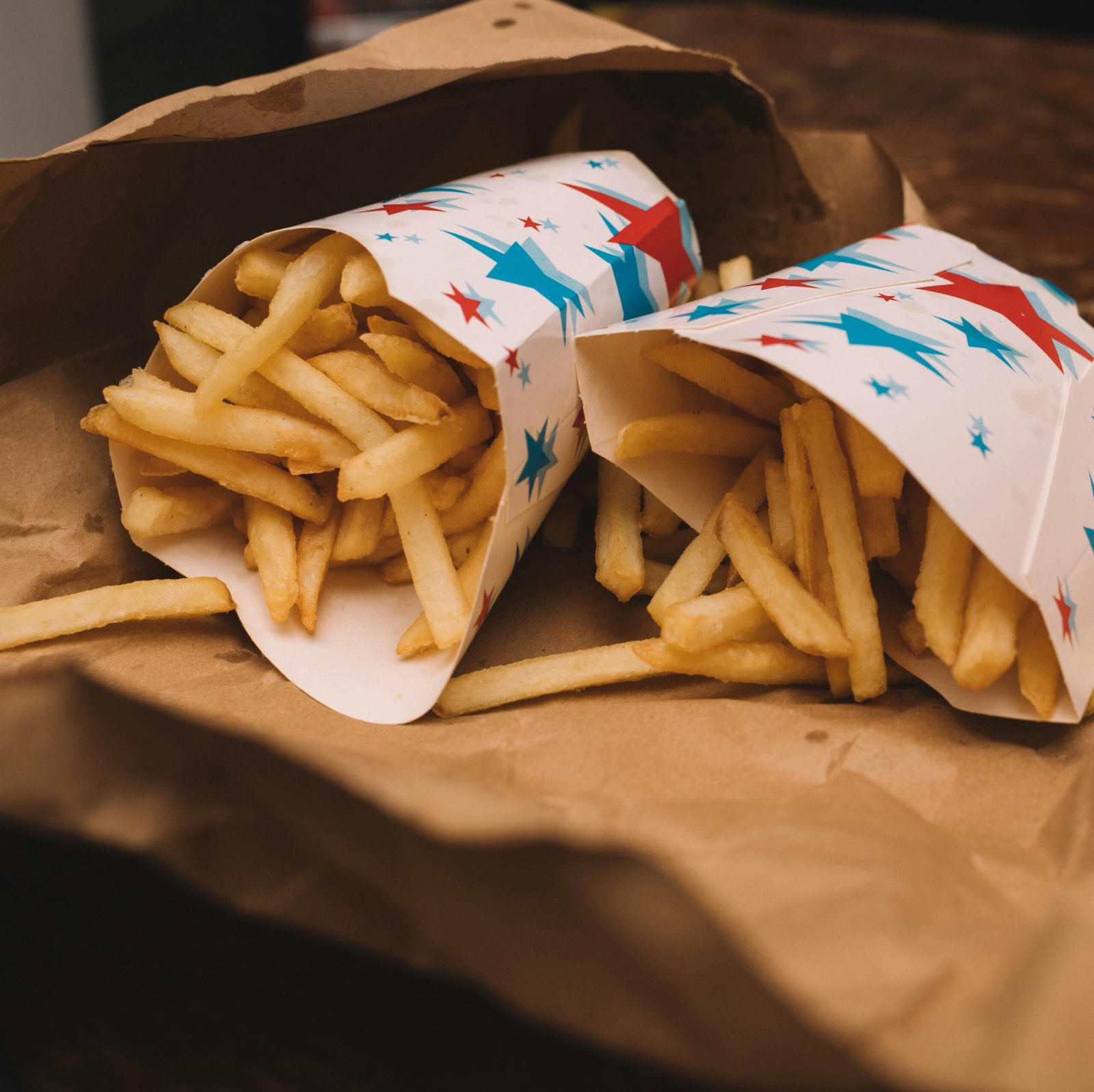 Golden crispy French fries in colorful star-patterned paper wrap on brown parchment.