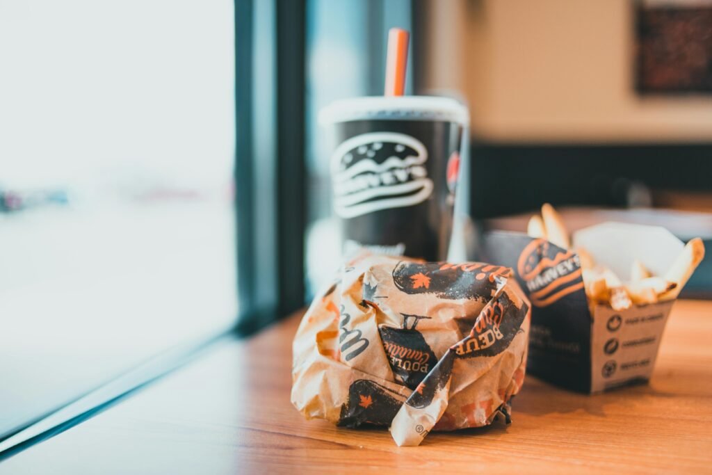 A wrapped burger, fries, and soda on a modern café table, indoors.