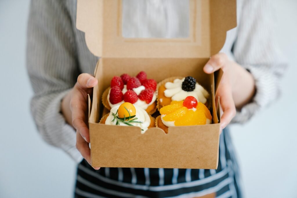Close-up of a woman holding a box filled with assorted fresh fruit cupcakes, perfect for dessert.