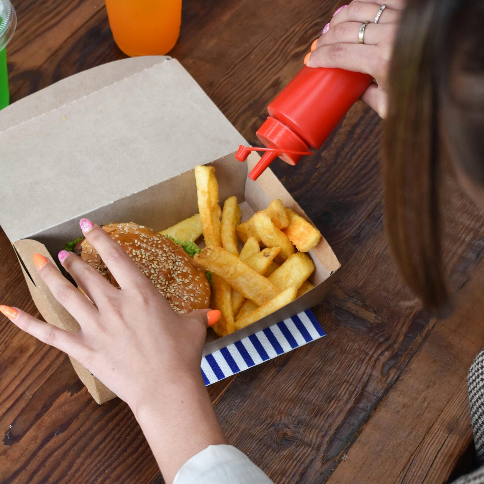 Overhead view of a woman adding ketchup to a burger and fries combo in a paper box.