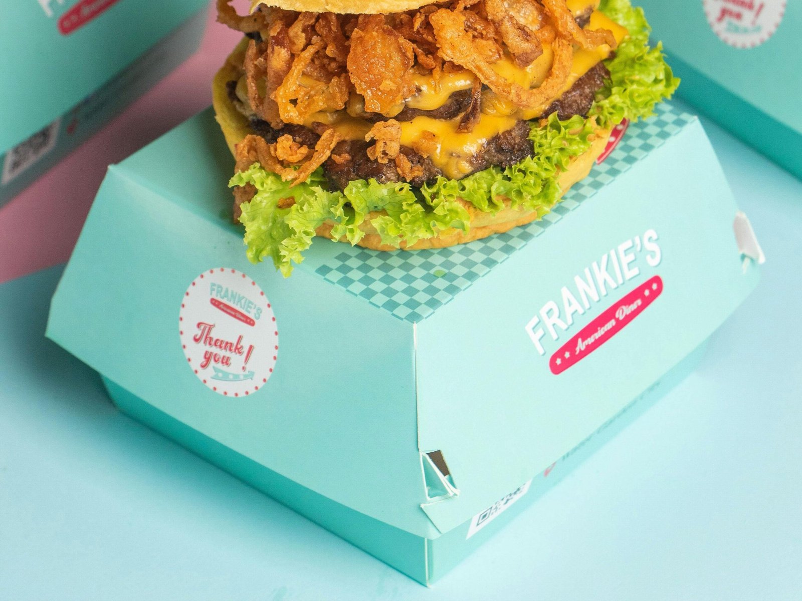 Close-up of a gourmet burger with onion rings and lettuce, served in a turquoise box.