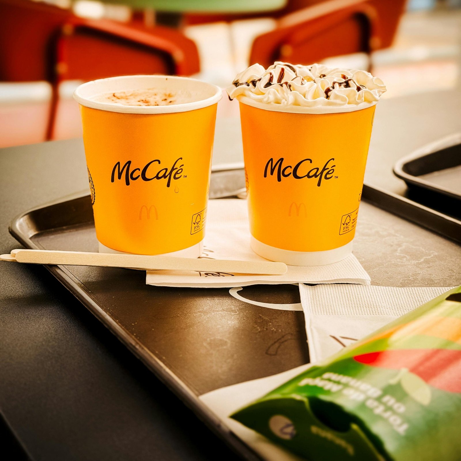 Two McCafé cups with whipped cream and napkins on a tray, highlighting dessert beverages in a São Paulo café.