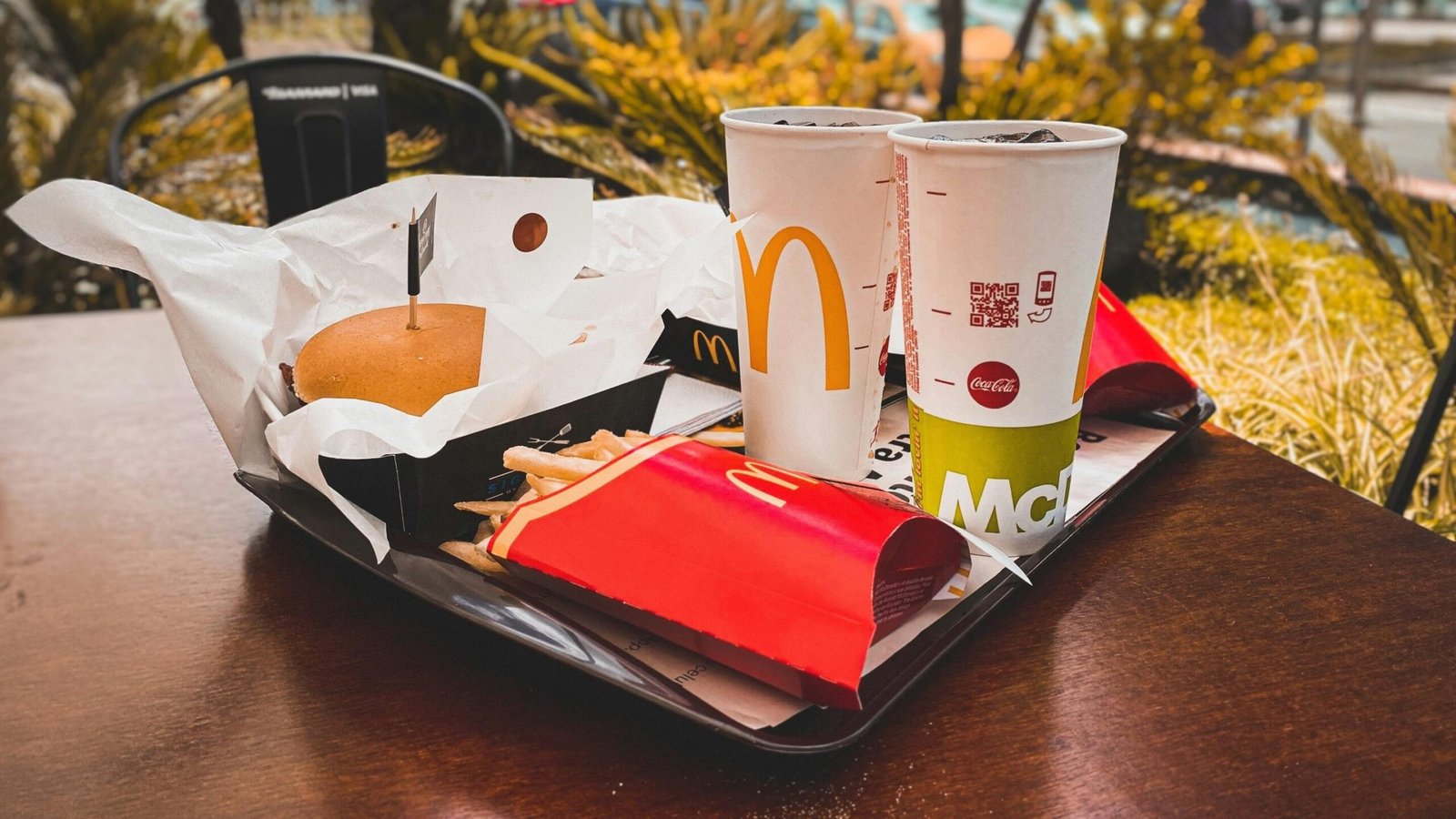 An appetizing fast food meal with burger, french fries, and drinks on an outdoor table in urban setting.