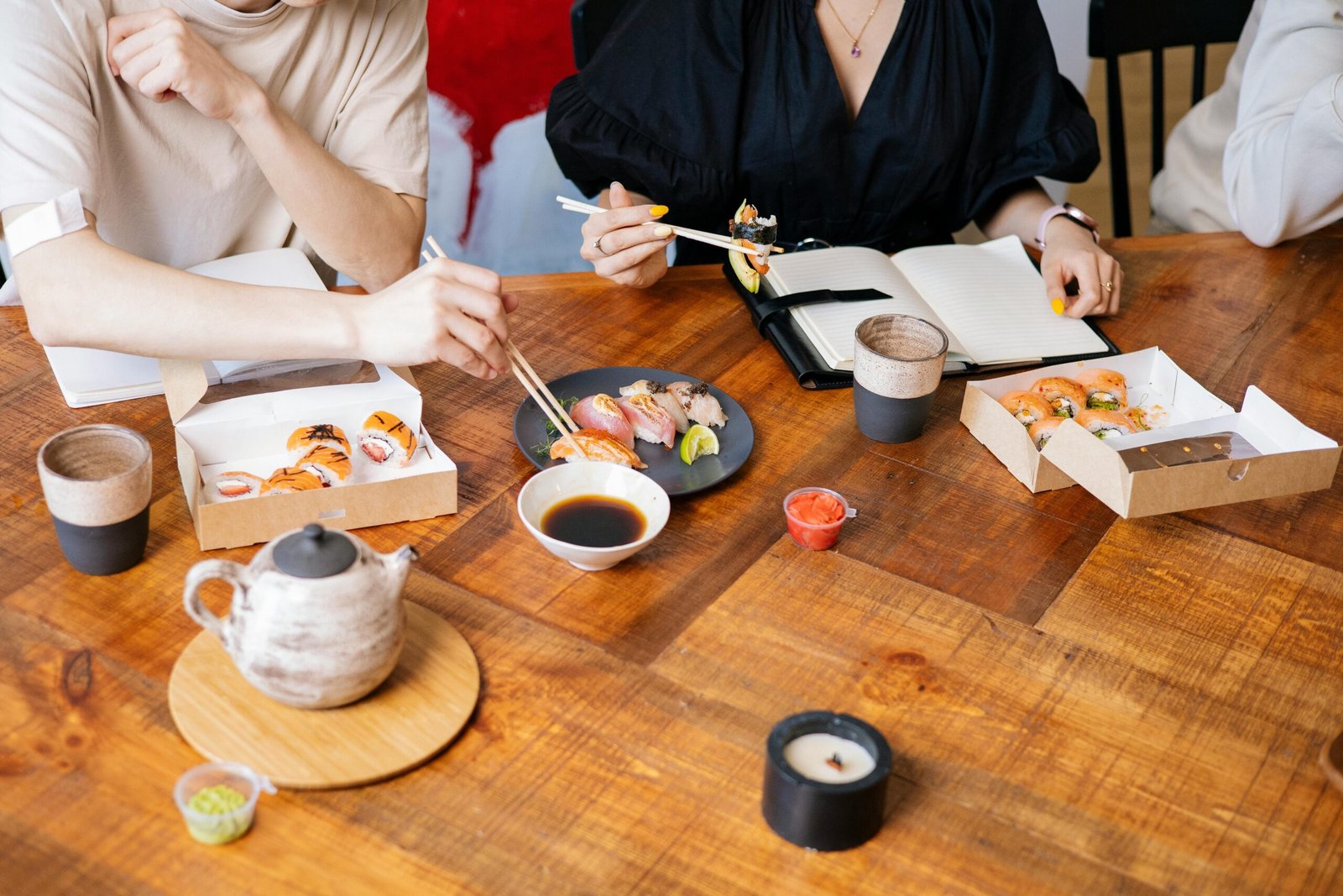 A group enjoying sushi at a café with takeout boxes on a wooden table.