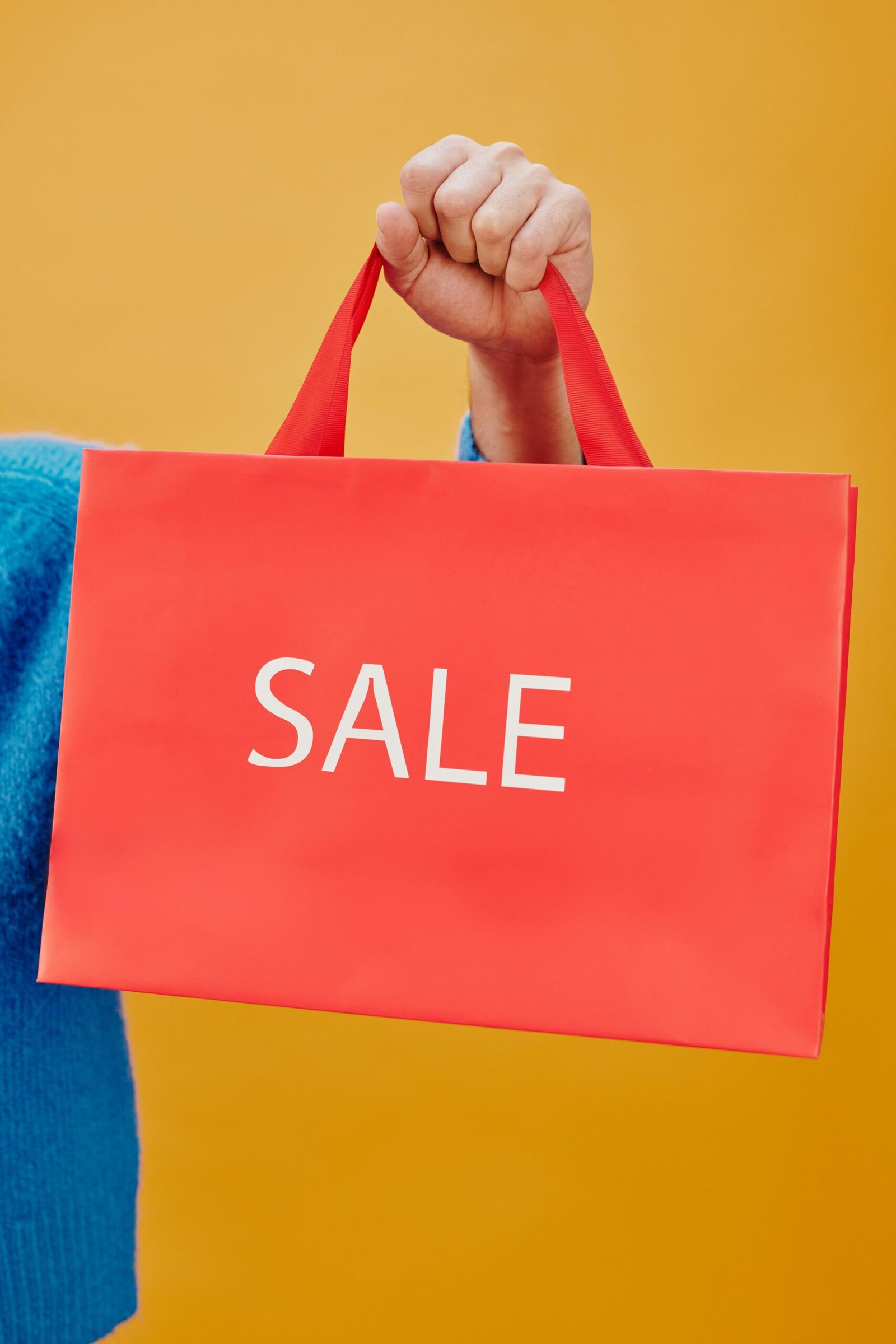 A red shopping bag with the word 'SALE' held against a vibrant yellow backdrop. Ideal for promotions.