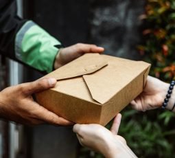 Close-up of a delivery person handing over a box to a customer outdoors.