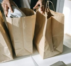 Adult organizing paper shopping bags next to a laptop and credit card on a white table.